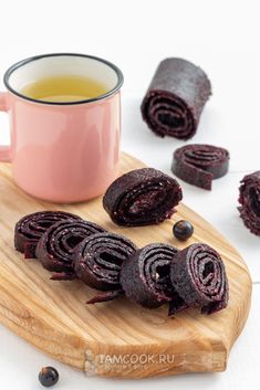 a wooden cutting board topped with cut up cookies next to a cup of tea