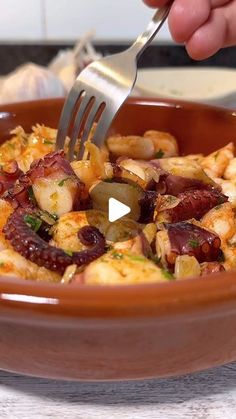 a person holding a fork in a bowl with shrimp and olives on the side