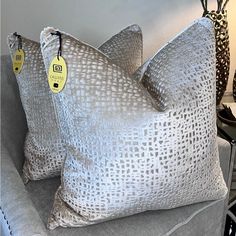 two gray pillows with tags on them sitting on a couch