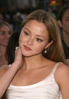 a beautiful young lady in a white dress posing for the camera with her hand on her chin