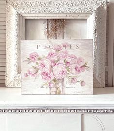 a white frame with pink flowers in it on top of a shelf next to a window