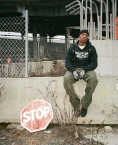 a man sitting on top of a cement wall next to a stop sign