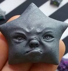 a hand holding a small gray star shaped object in it's right hand, with the face of an alien