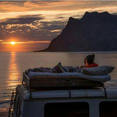 a person sitting on top of a boat in the water at sunset with mountains in the background