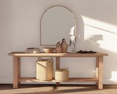 a wooden table topped with baskets next to a mirror and bowl on top of it