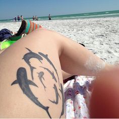 a person with a dolphin tattoo on their back laying in the sand at the beach