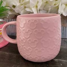 a pink mug sitting on top of a table next to white flowers