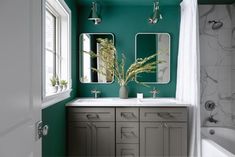 a bathroom with green walls and two mirrors on the wall, along with a white bathtub