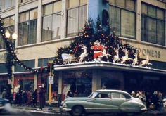 an old car driving down the street in front of a building decorated with christmas lights