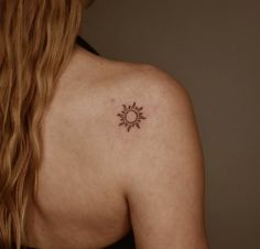 the back of a woman's shoulder with a small sun tattoo