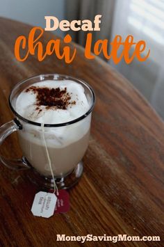 a glass mug filled with hot chocolate and whipped cream on top of a wooden table