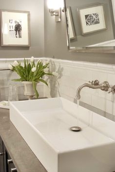 a white sink sitting under a bathroom mirror next to a vase with flowers in it