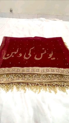 a red and gold shawl with arabic writing on the front, sitting on a bed