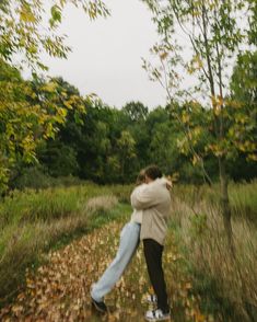 two people hugging each other in the middle of a field with leaves on the ground