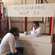 two men sitting at a counter talking to each other in front of a sign that says psychic help 54