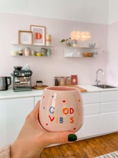 a woman holding up a pink cup with the words good vibes painted on it