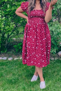 a woman in a red dress is standing on the grass with her hands behind her head