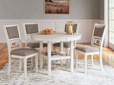 a white table with four chairs and a bowl of fruit on top of the table