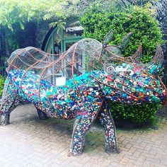 a sculpture of a horse made out of bottle caps in front of some bushes and trees