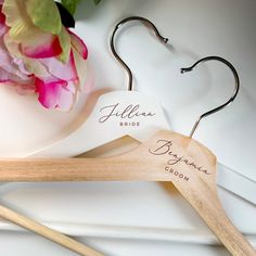 a pair of wooden clothes hangers with personalized names on them and flowers in the background