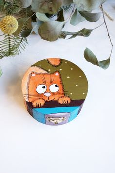 an orange cat sitting on top of a wooden box next to some green leaves and flowers