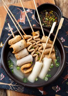 a bowl filled with food on top of a wooden table next to dipping sauce and chopsticks