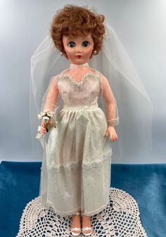 a doll wearing a wedding dress and veil on top of a doily with a blue background