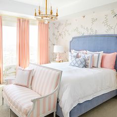 a bedroom decorated in pink and white with a blue headboard, striped upholstered chair, and chandelier