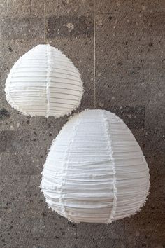 two white paper lanterns hanging from strings on concrete floor with cement wall in the background