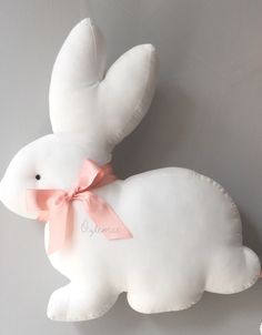 a white stuffed animal with a pink ribbon on it's neck and ears is laying next to a gray wall