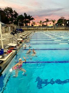 people are swimming in the pool at sunset