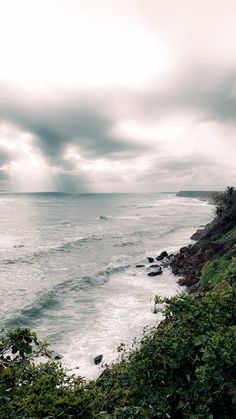 an ocean view with waves crashing on the shore and dark clouds in the sky above