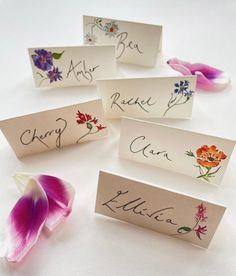 four place cards with flowers on them and the name of each card in cursive writing