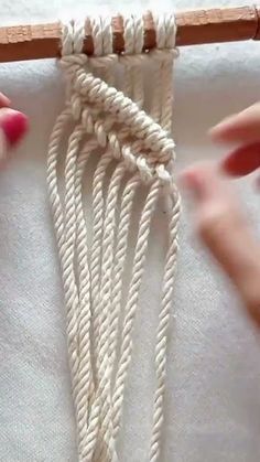 two hands are working on an object with white yarn and wood dows in the background