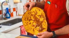 a man in an orange apron is holding a large piece of food