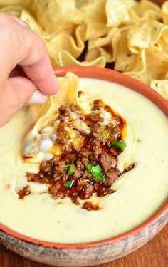 a hand dipping tortilla chips into a bowl filled with cheese and ground beef