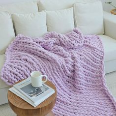 a coffee cup on a table next to a pink blanket and white couch in a living room