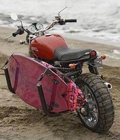 a red motorcycle parked on top of a sandy beach