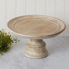 a white cake plate sitting on top of a table next to a potted plant