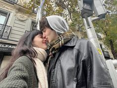 a man and woman standing next to each other near a street light with trees in the background