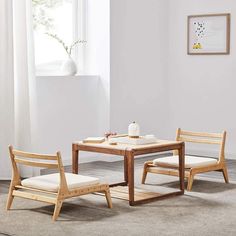 two wooden chairs and a table in a room with white walls, rugs and windows