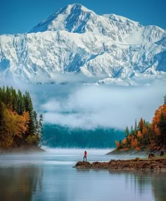 a person standing on a rock in the middle of a lake with mountains in the background