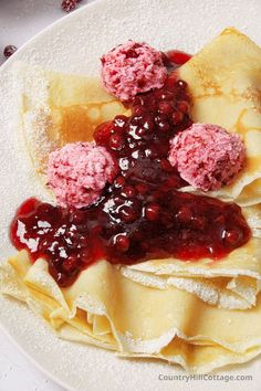 crepes with raspberry sauce and powdered sugar on top are served on a white plate