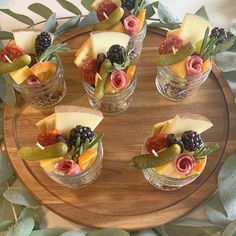 fruit and cheese appetizers are arranged in small glass dishes on a wooden platter