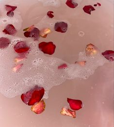 rose petals floating in water with bubbles on the bottom and pink liquid around them,