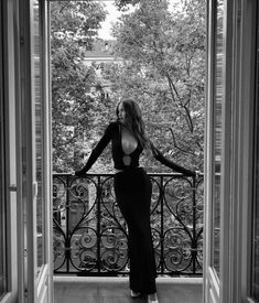 black and white photo of woman in long dress standing on balcony with trees behind her