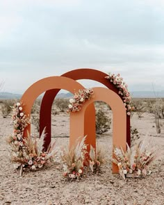 an arch decorated with flowers sits in the middle of a desert landscape, surrounded by dry grass and tall grasses