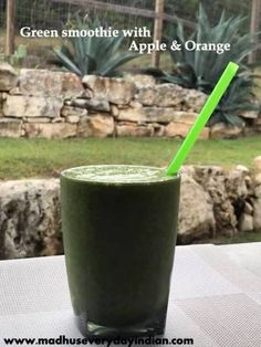 a green smoothie with an apple and orange straw in it sitting on a table