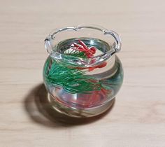 a small glass vase filled with red and green plants on top of a wooden table