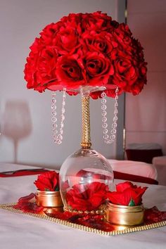 red roses are in a glass vase on a table with gold trays and candles